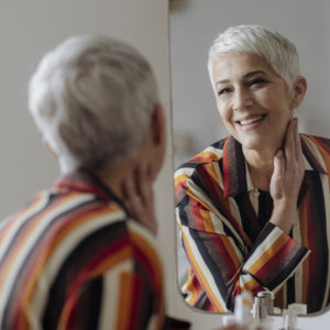 Beautiful smiling grey-haired smiling woman looking herself in the mirror after microdermabrasion.