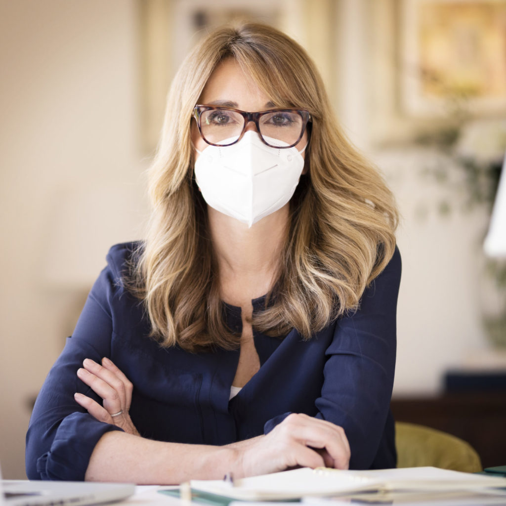 Portrait shot of middle aged woman wearing face mask while working at home on her notebook and text messaging during coronavirus pandemic.