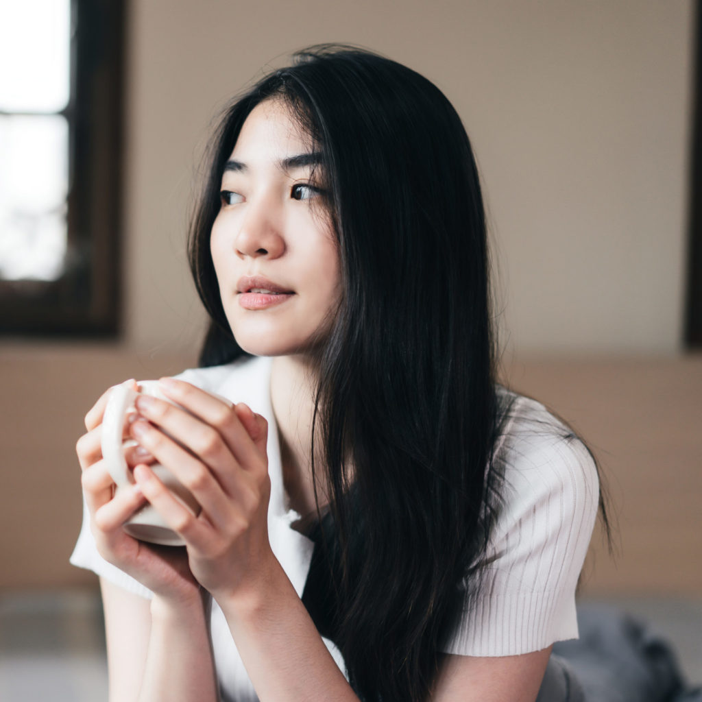 Young asian adult woman hold cup of coffee in the morning in bed room at home.