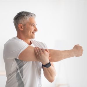 Sporty Mature Man Stretching Hands after home workout.