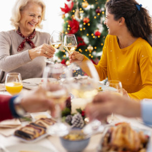 Family having Christmas dinner at home, gathered around the table, enjoying their time together; mother and daughter making a toast raising glasses of wine
