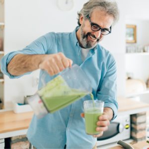 Mature Man pouring a green smoothie in the kitchen.