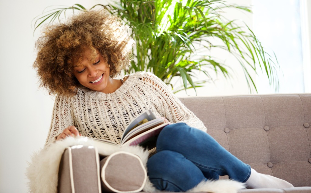 Attractive African American Woman Sitting On Sofa Reading Book