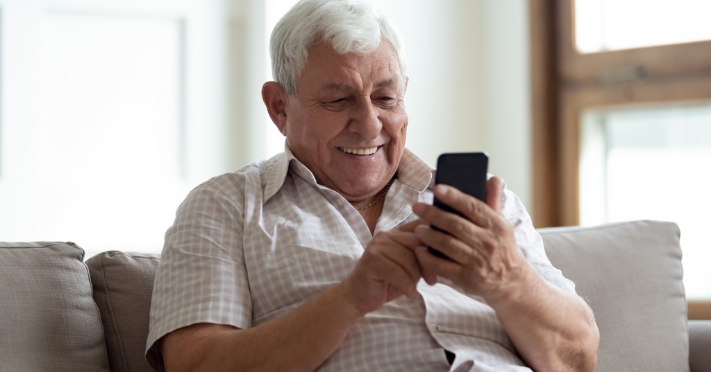 Happy Older Man Sitting On Sofa At Home Using Smartphone Picture Id1189748843