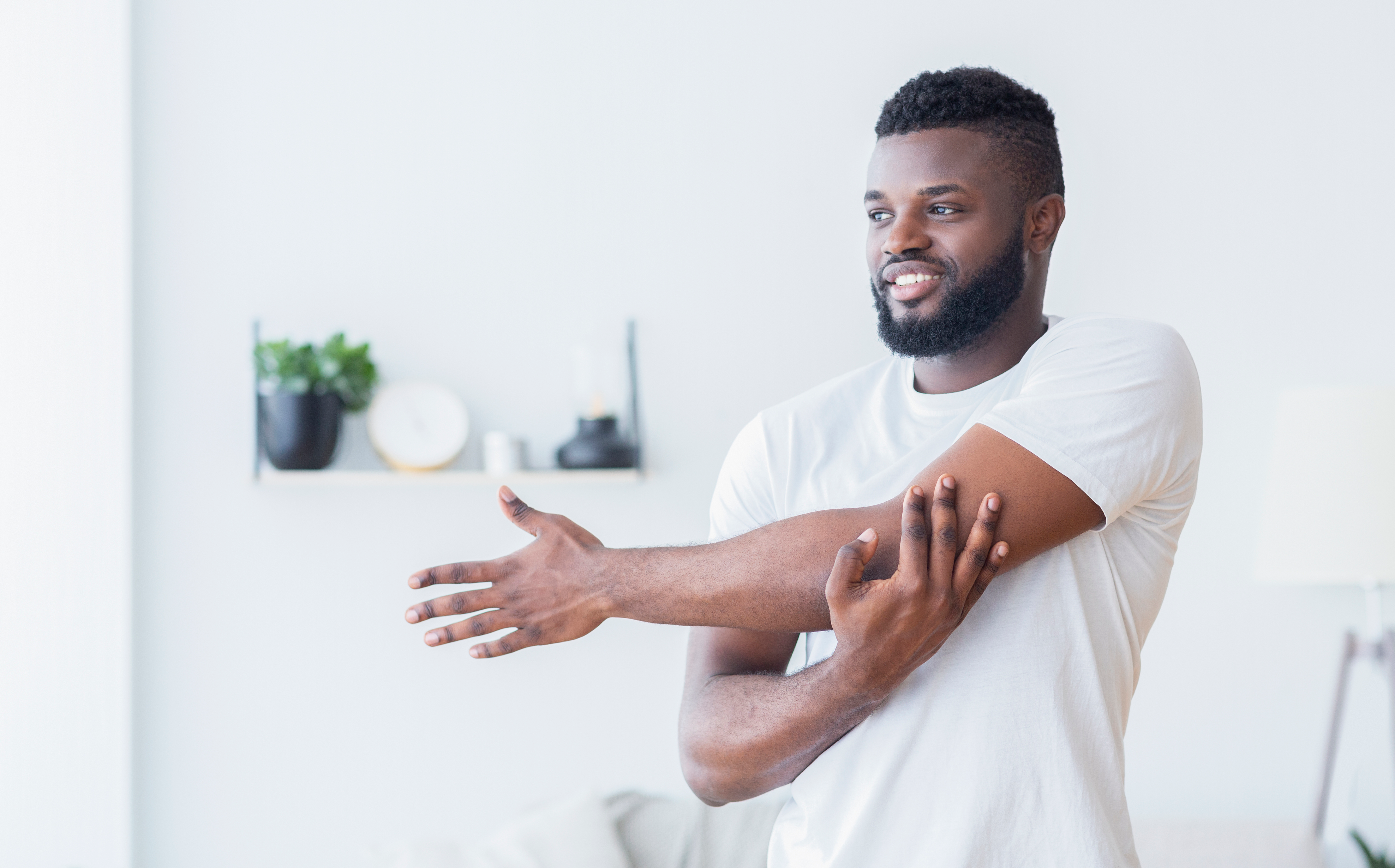 Young black man training and stretching arm at home