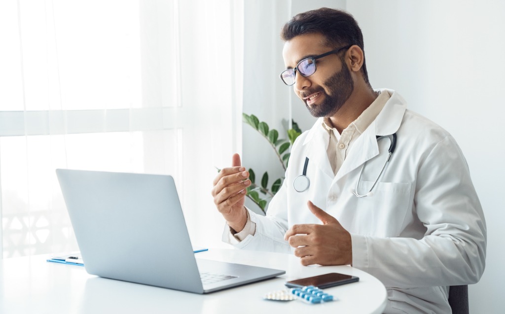 Portrait Of Indian Man Doctor Talking To Online Patient On Laptop Picture Id1329697243