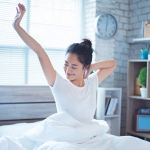 Woman stretching in bed after waking up after a good night's sleep.