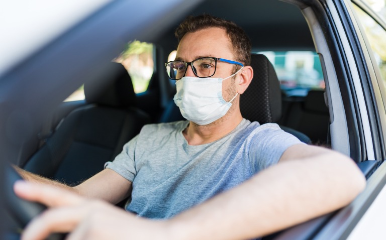 Portrait of man wearing surgical mask while driving a car.