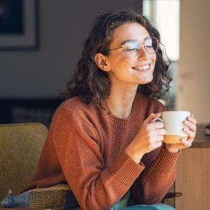 Peaceful woman drinking warm drink in mug, smiling with eyes closed in a calm mental state.