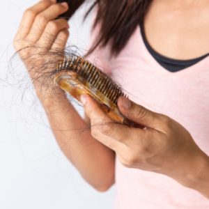 Woman holding brush full of hair while suffering from hair loss.