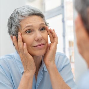 Mature woman admiring skin in mirror after receiving PRP Therapy