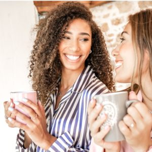 Multiracial Women Couple Smiling Looking Each Other Holding A Teacup