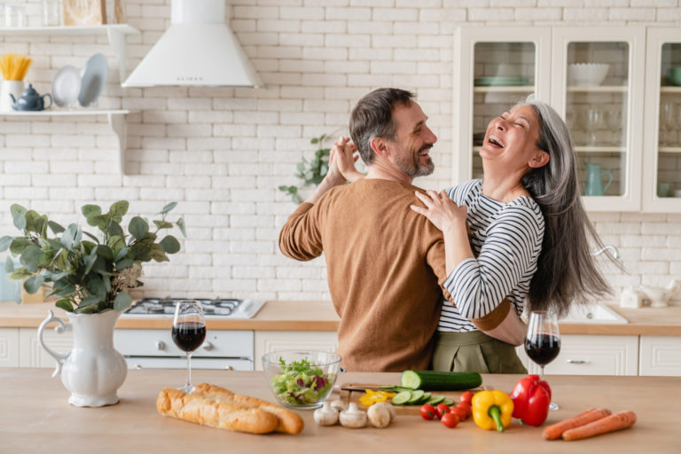 Happy cheerful middle-aged mature couple family parents dancing together in the kitchen, preparing cooking food meal for romantic dinner, spending time together.