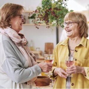 Senior Women Talking To Each Other while holding stem glasses partially filled with rose colored liquid.