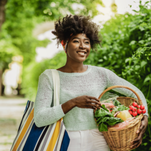 Smiling woman walking outdoors holding a basket of fresh produce.