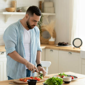 Millennial man stand at modern kitchen table chop vegetables prepare fresh vegetable salad for dinner or lunch, young male cooking at home make breakfast follow healthy diet, vegetarian concept